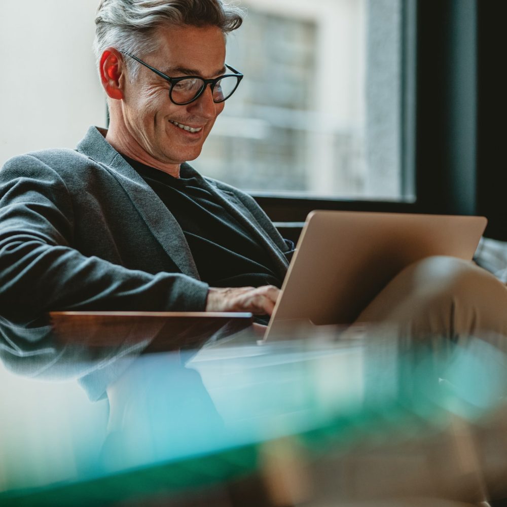 Smiling businessman sitting in office lobby working on laptop. Male business professional working in office lobby.